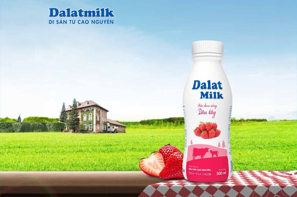 Chai sữa chua uống Dalat Milk dâu tây 500ml trên cánh đồng cỏ, phía sau là nhà máy sữa dalat milk